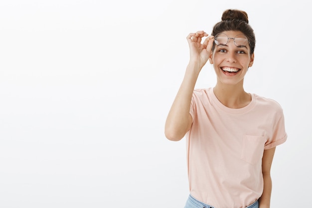 Enthousiaste jeune femme élégante posant contre le mur blanc