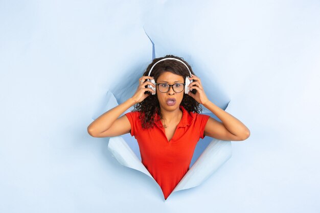 Enthousiaste jeune femme pose en fond de trou de papier bleu déchiré, émotionnel et expressif