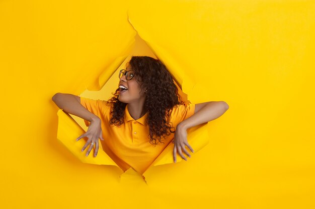 Enthousiaste jeune femme pose en fond de trou de papier jaune déchiré, émotionnel et expressif