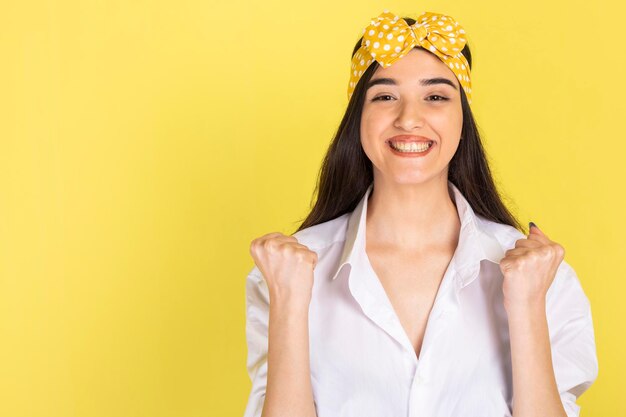 Enthousiaste jeune femme serrant ses poings et souriant sur fond jaune Photo de haute qualité