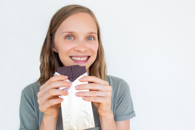 Enthousiaste jeune femme tenant une barre de chocolat en feuille d'or