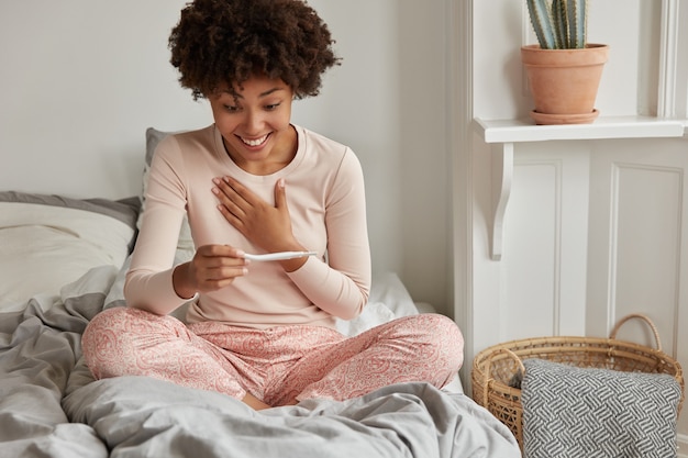 Enthousiaste jeune femme avec test de grossesse posant à la maison