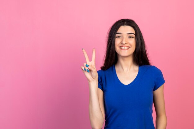 Enthousiaste jeune fille geste paix et souriant sur fond rose Photo de haute qualité