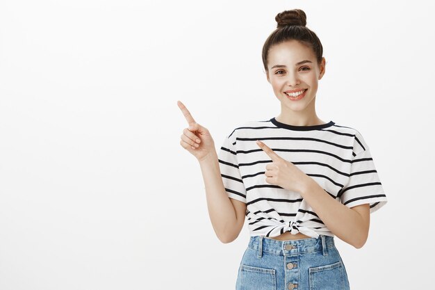 Enthousiaste jolie brune souriant largement, pointant le doigt dans le coin supérieur gauche