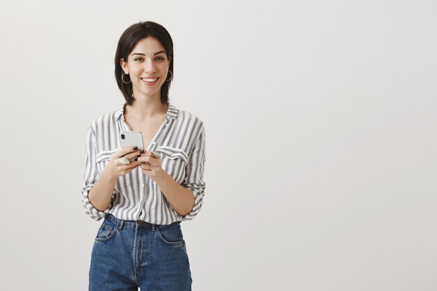 Enthousiaste jolie fille à l'aide de téléphone portable et souriant