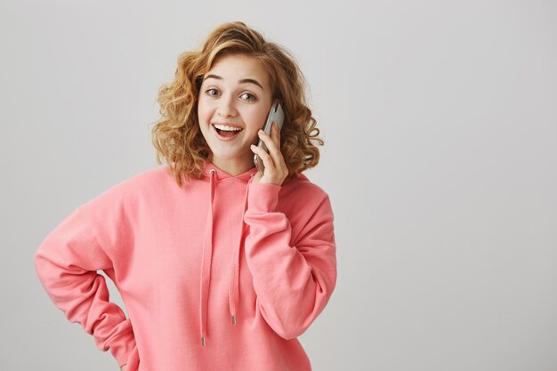 Enthousiaste jolie jeune fille parlant au téléphone et souriant