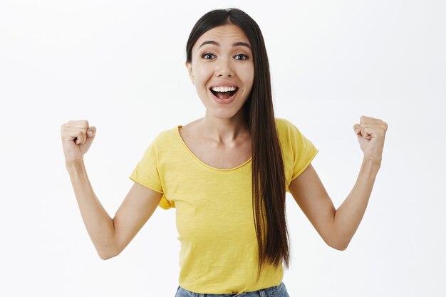 Enthousiaste et optimiste femme européenne attrayante avec de longs cheveux foncés levant le poing gaiement