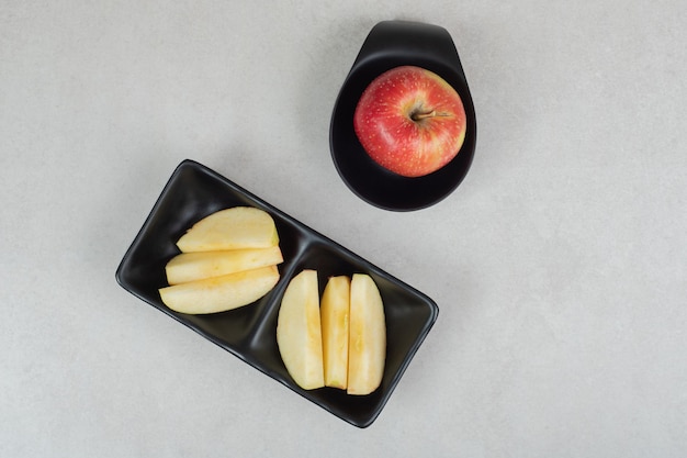 Entier et tranches de pomme rouge sur assiettes noires.