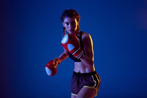 Entraine toi. Fit femme caucasienne en boxe sportswear sur fond bleu en néon.