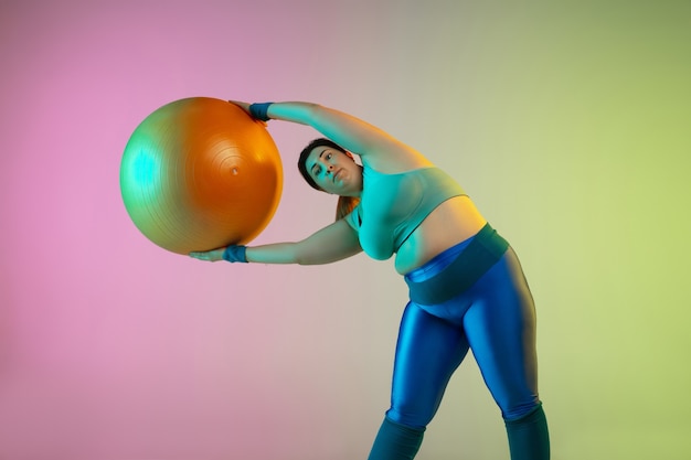 Entraînement d'un jeune mannequin de taille plus caucasienne sur un mur vert violet dégradé à la lumière du néon.