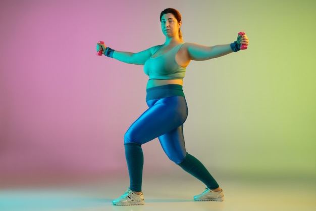 Entraînement d'un jeune modèle féminin de taille plus caucasienne sur un mur vert violet dégradé