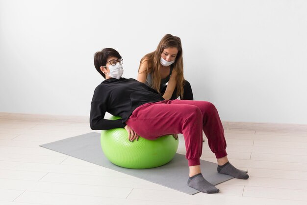 Un entraîneur aide une femme à se remettre d'un coronavirus avec un ballon de fitness