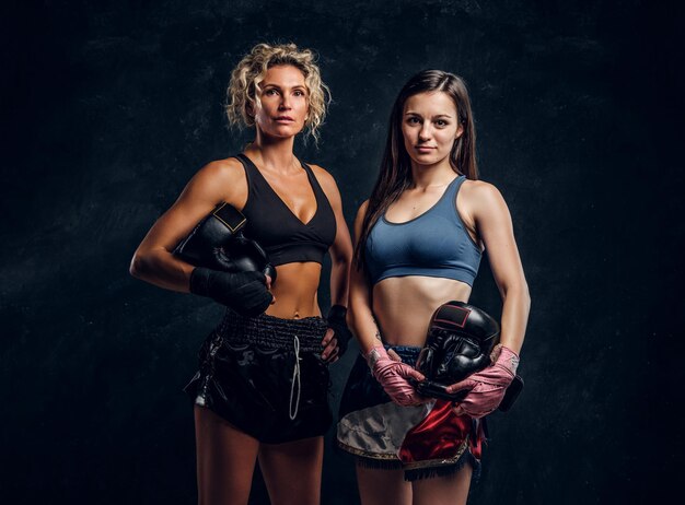 Un entraîneur de boxe expérimenté et son jeune étudiant posent pour un photographe dans un studio photo sombre.