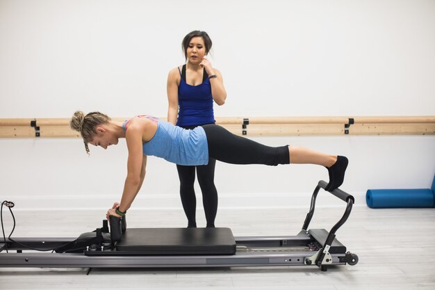 Entraîneur féminin aidant femme avec exercice d'étirement sur réformateur