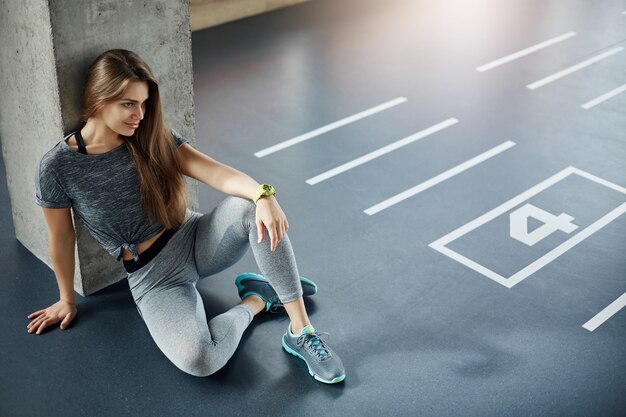 Entraîneur de femme de remise en forme du corps assis sur le sol du gymnase, planifier sa nouvelle session de formation. Biceps et triceps forts.