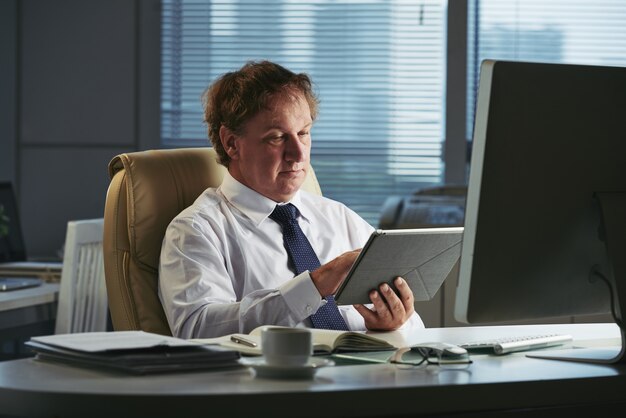 Entrepreneur d'âge moyen lisant les nouvelles mondiales en ligne sur sa tablette PC