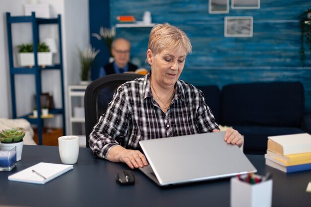 Entrepreneur mûr assis devant un ordinateur portable au bureau. Femme âgée dans le salon de la maison à l'aide d'un ordinateur portable à technologie moderne pour la communication assise au bureau à l'intérieur.