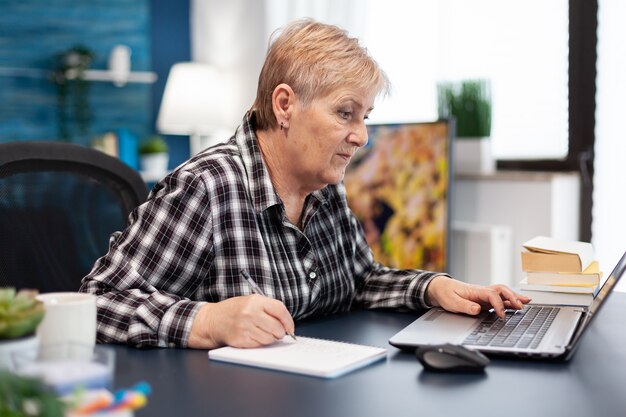Entrepreneur mûr prenant des notes sur un ordinateur portable travaillant au bureau à domicile