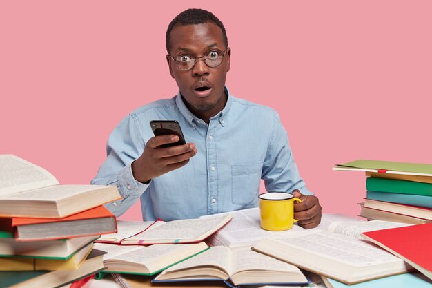 Un entrepreneur à la peau sombre tient un téléphone portable dans une main et une tasse de café dans l'autre, vêtu de vêtements formels