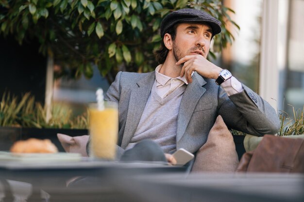 Entrepreneur pensif avec téléphone portable assis dans un café et pensant à quelque chose