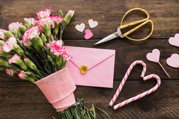 Enveloppe près du bouquet de fleurs avec ruban, ciseaux et cannes de bonbon