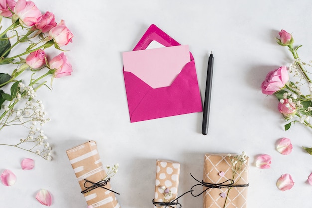 Photo gratuite enveloppe près du stylo, roses fraîches et cadeaux