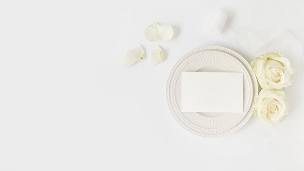 Enveloppe vierge sur assiette avec des roses et ruban enroulé sur fond blanc