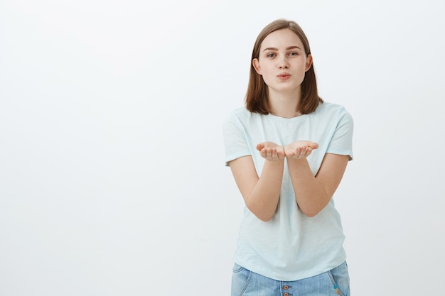 Envoi de doux baiser par voie aérienne. Portrait de charmante femme mignonne insouciante en t-shirt à la mode se penchant vers avec les paumes ouvertes près de la poitrine pliant les lèvres pour souffler mwah souriant timide