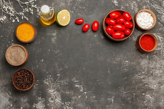 épices et bols à vaisselle d'épices colorées bouteille d'huile citron et tomates sur la table sombre