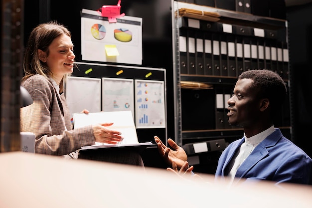 Photo gratuite Équipe discutant du rapport de comptabilité, travaillant tard dans la nuit à l'enregistrement de la bureaucratie dans la salle d'entreposage. divers employés de dépôt analysant les documents administratifs, découvrant les fichiers comptables