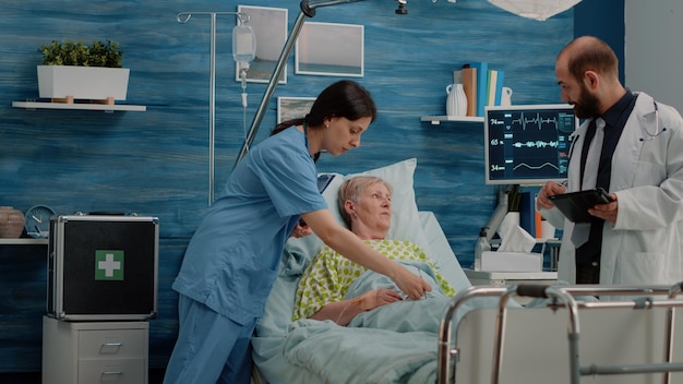 Équipe médicale consultant un patient malade au lit dans une maison de soins infirmiers. médecin faisant un bilan de santé pour une femme âgée pendant qu'une infirmière utilise un oxymètre pour la saturation en oxygène. examen de santé