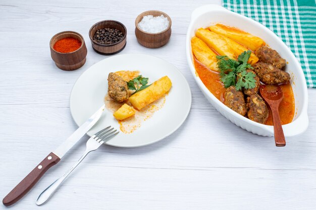 Escalopes de viande cuites avec pommes de terre en sauce et assaisonnements verts sur un bureau blanc, légume de viande de repas alimentaire