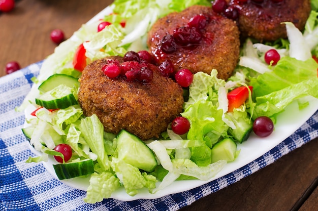 Escalopes de viande juteuse avec sauce aux canneberges et salade sur une table en bois dans un style rustique.