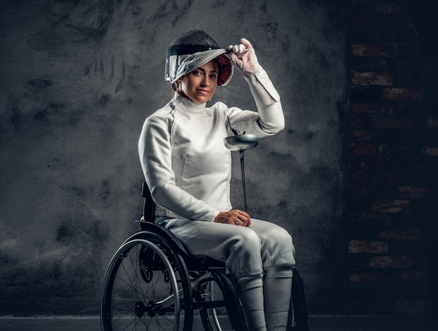 L'escrimeuse en fauteuil roulant tient un masque de sécurité et une épée.