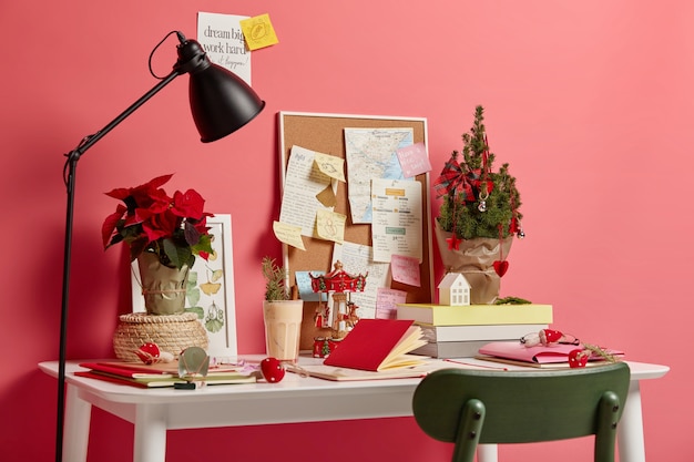 Photo gratuite espace de travail confortable sans personne. bureau blanc avec blocs-notes, lampe, petit sapin de noël décoré symbolisant les vacances à venir