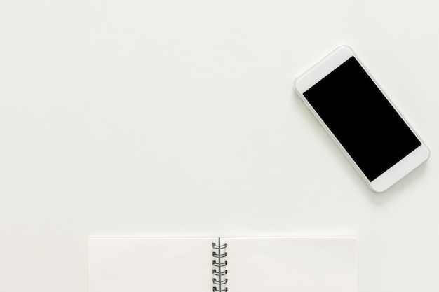 Espace de travail minimal - Photo de bureau de travail créative avec un carnet de croquis et un téléphone portable avec écran vierge sur fond blanc de copie. Vue de dessus, photographie plate.