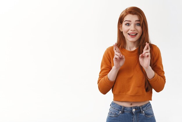 Espoir heureux joyeux fille rousse urbaine porter un chandail recadré croiser les doigts bonne chance souriant anticipant des nouvelles positives priant rêve devenu réalité en attente de miracle souhait réaliser fond blanc