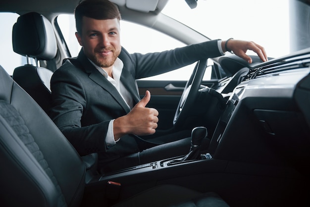 C'est génial. Homme d'affaires moderne essayant sa nouvelle voiture dans le salon automobile