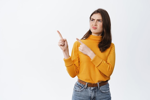 Photo gratuite c'est grossier jeune femme dégoûtée fronçant les sourcils pointant du doigt et regardant à gauche une mauvaise chose dégoûtante n'aime pas et condamne quelque chose debout sur fond blanc