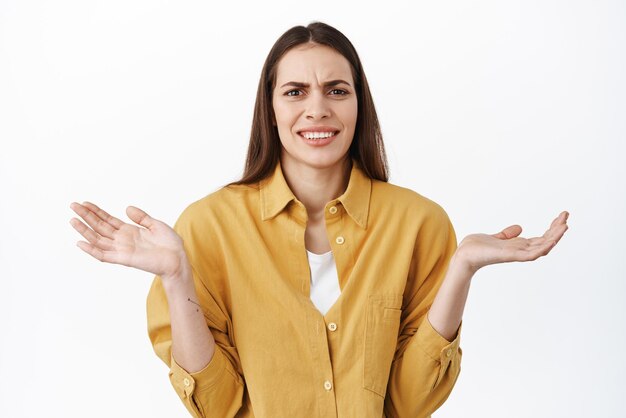 C'est un non-sens ridicule Une femme confuse et agacée écarte les mains sur le côté en haussant les épaules et en grimaçant dérangée ne peut pas comprendre ce qui compte pourquoi bien que debout sur fond blanc