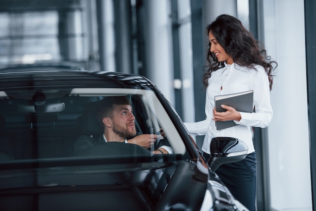 C'est à toi maintenant. Client masculin et femme d'affaires moderne dans le salon automobile