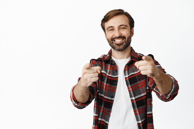 Photo gratuite c'est vous félicitations un barbu souriant pointant du doigt la caméra vous loue en choisissant le candidat invitant les gens debout sur fond blanc