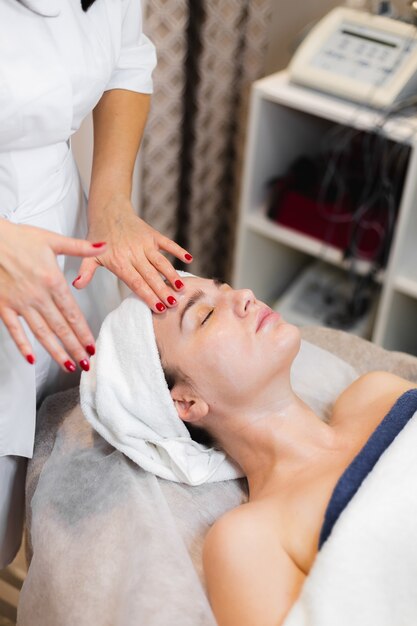 Esthéticienne dans un salon de beauté spa applique la crème sur le visage d'un client, une fille se trouve sur une table de cosmétologie