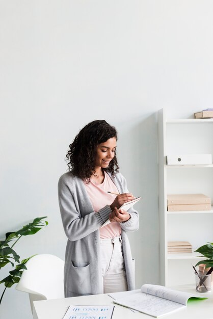 Ethnique jeune femme écrivant sur le presse-papiers au bureau