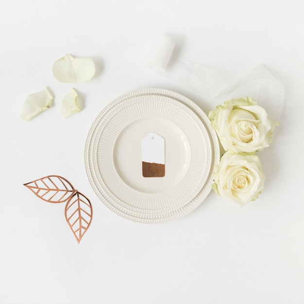 Photo gratuite Étiquette vierge sur plaque blanche avec rose; feuilles et ruban sur fond blanc
