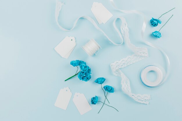 Étiquettes blanches; ruban de dentelle; bobine et roses bleues sur fond coloré