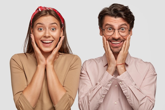 Photo gratuite Étonné jeune couple posant contre le mur blanc