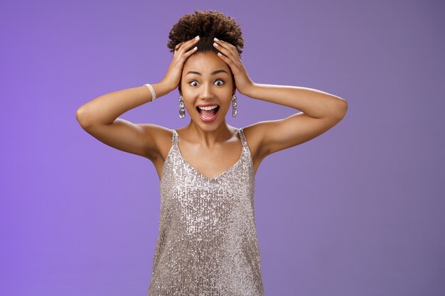 Photo gratuite Étonné surpris excité femme aricano-américaine gagnante à la loterie ne peut pas croire ravi tenir la tête crier amusé souriant étonné debout impressionné dans une robe brillante scintillante, fond bleu.