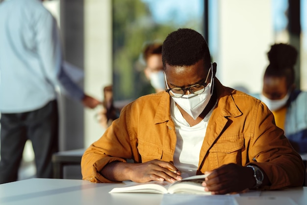 Photo gratuite Étudiant afro-américain avec masque facial lisant un livre en classe