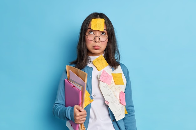 Un étudiant asiatique fatigué malheureux concentré ci-dessus a une expression triste porte des lunettes pour la correction de la vue détient des dossiers papiers collés avec des trombones.